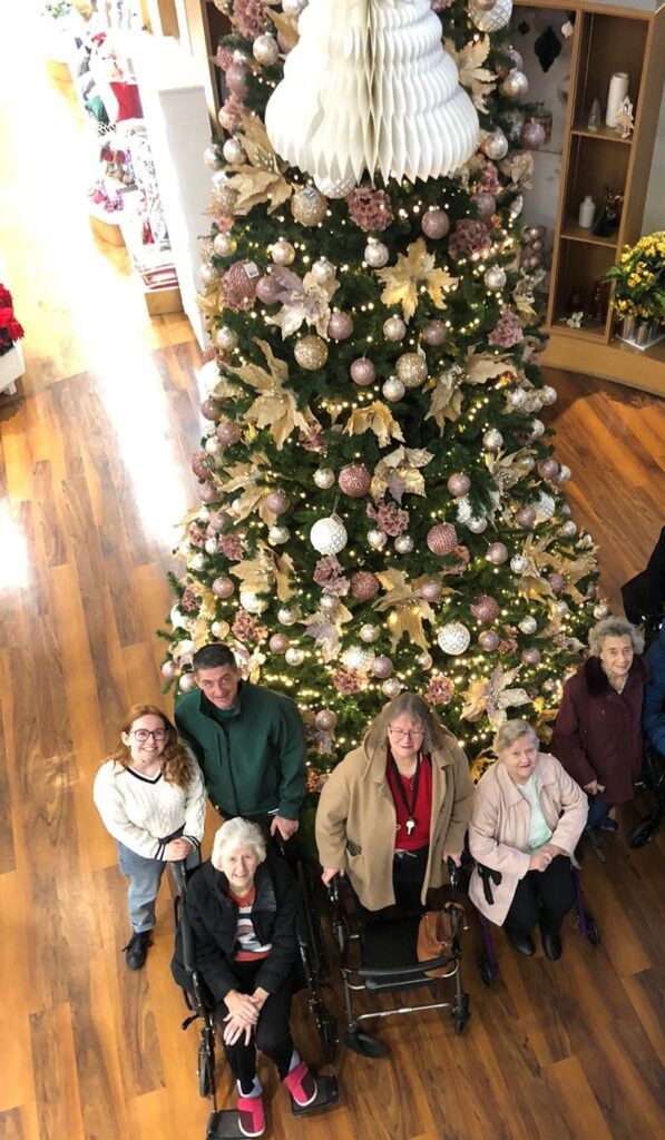 Residents and Staff Standing by Large Christmas Tree